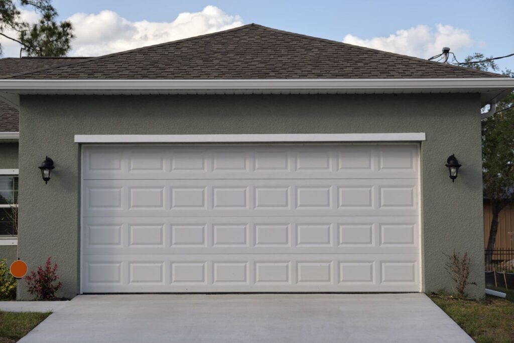 White raised panel double garage door on a green stucco house with concrete driveway