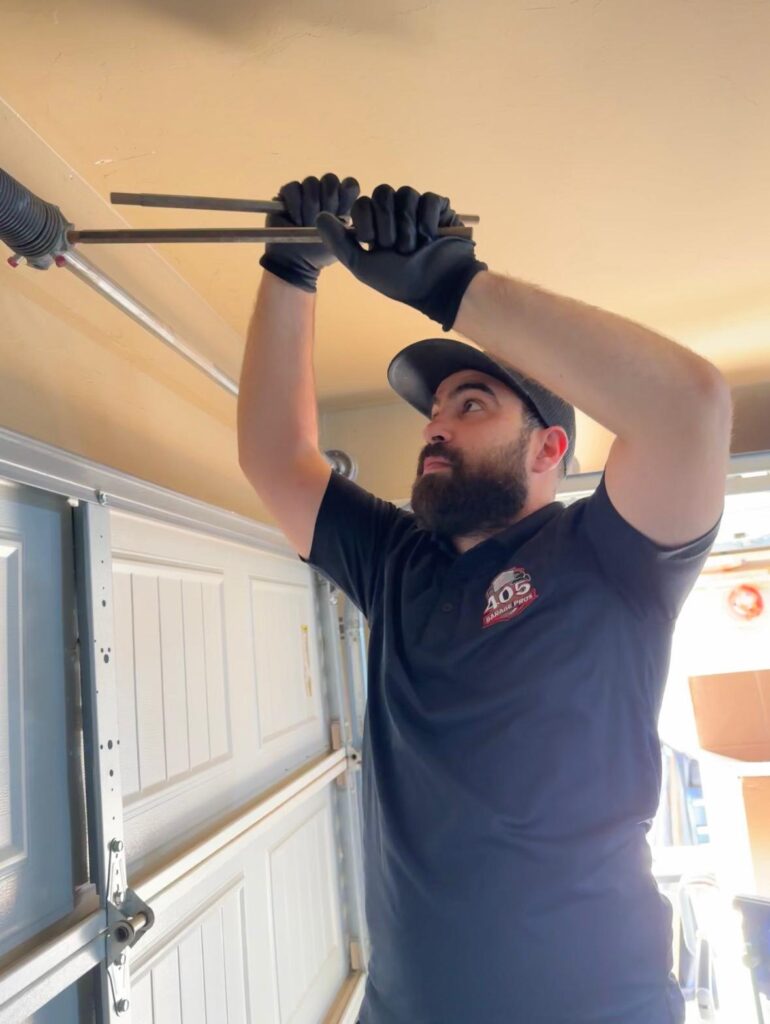 Technician from 405 Garage Pros adjusting a garage door torsion spring with winding bars inside a residential garage in Edmond, OK.