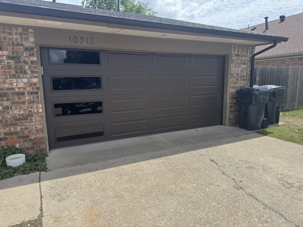 Brown raised panel residential garage door with window inserts on a brick home